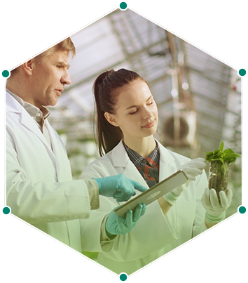 a male and female wearing lab coats examining a plant